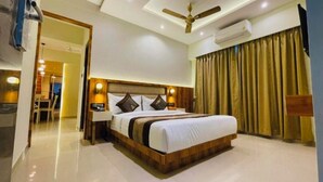 A hotel room with a large bed, a ceiling fan, an air conditioning unit, and a view of a dining area. - The Grace b&B (New Delhi)