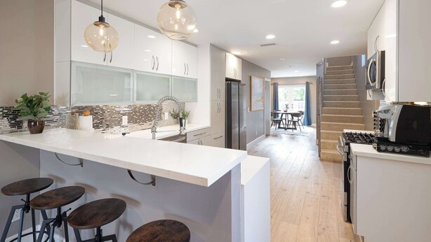 Een moderne keuken met een wit aanrecht, barstoelen en hanglampen.