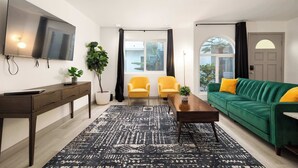 Un salon moderne avec un téléviseur à écran plat, un canapé vert agrémenté de coussins jaunes, deux fauteuils jaunes, une table basse en bois et un tapis à motifs.