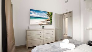 Une chambre à coucher avec un lit, une commode, un tableau représentant une plage et une porte.