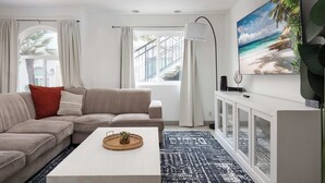 Un salon moderne avec un canapé d’angle beige, une table basse blanche et un grand tableau sur le thème de la plage accroché au mur.