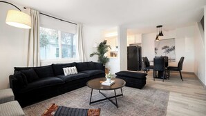 A modern living room with a black sofa, a round coffee table, and a dining area with a black table and chairs.