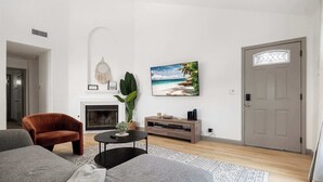A modern living room with a fireplace, a large painting of a beach, and a door with a window.