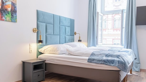 A bedroom with a bed, bedside tables, a window with curtains, and a wall-mounted light fixture. - Chic 1BR Apt Walk to Vienna Sights (Vienna)