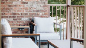 A patio with two chairs and a table, a brick wall, and a metal railing.