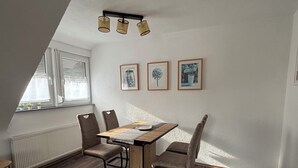 A dining area with a wooden table, four chairs, and a window with blinds. - Charming vacation apartment - quiet surroundings but close to the city (Deutschland)
