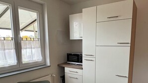 A compact kitchen with white cabinets, a microwave, and a window with curtains. - Charming vacation apartment - quiet surroundings but close to the city (Deutschland)
