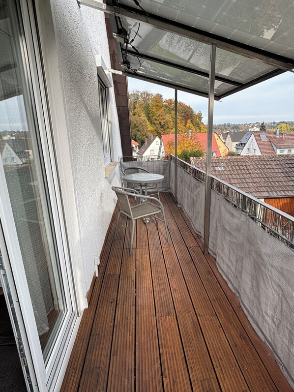 A balcony with a wooden floor, a table, and two chairs. - Charming vacation apartment - quiet surroundings but close to the city (Deutschland)