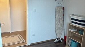A room with a wooden floor, a door leading to another room, a standing iron, and a shelf with storage bins. - Charming vacation apartment - quiet surroundings but close to the city (Deutschland)