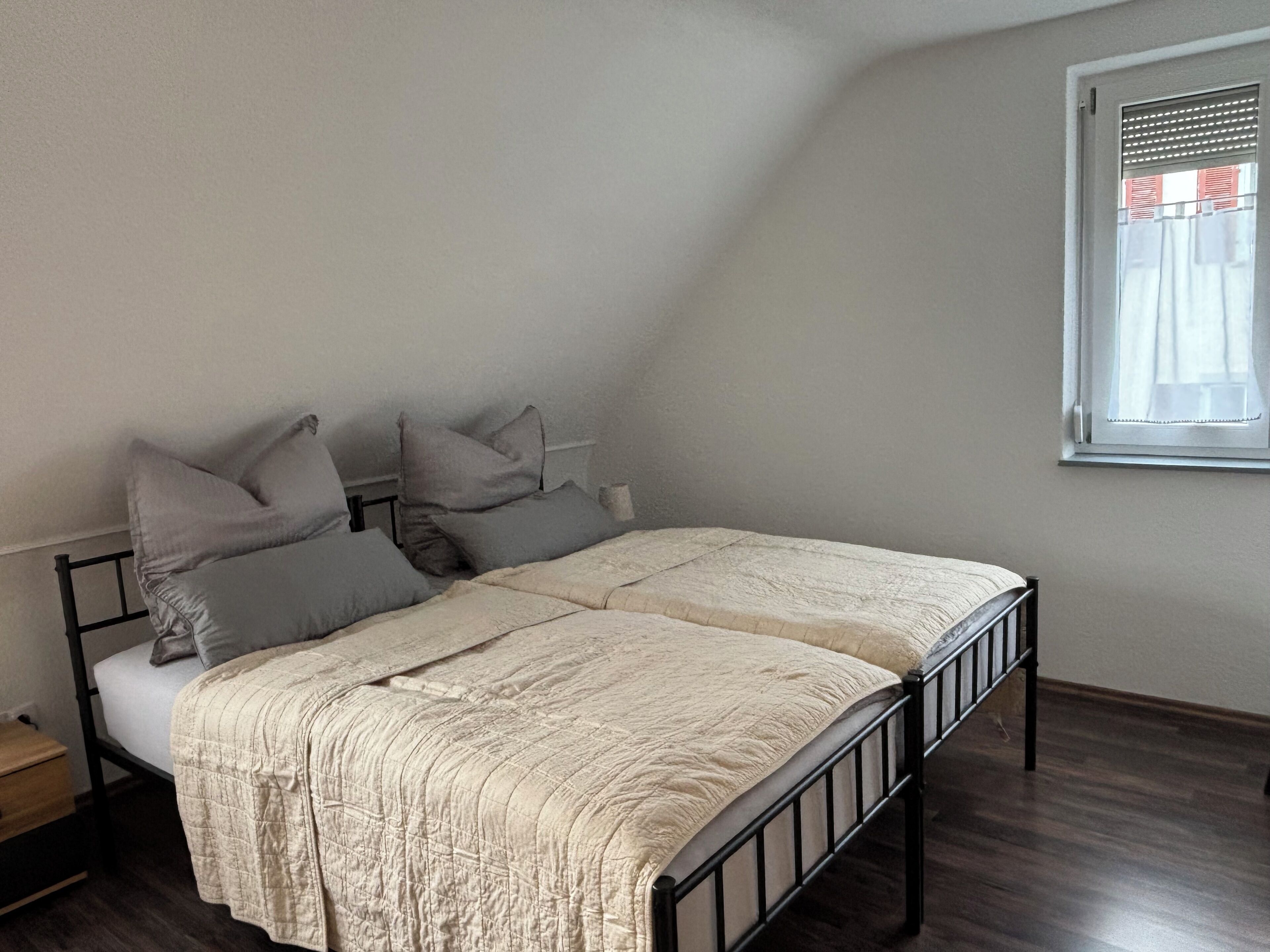 A single bed with a headboard, a bedside table, and a window with blinds.
