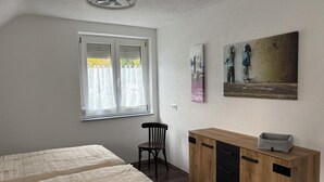 A bedroom with two beds, a wooden cabinet, a chair, and a window with blinds. - Charming vacation apartment - quiet surroundings but close to the city (Deutschland)
