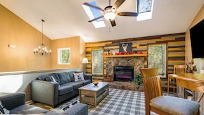 A cozy living room with a fireplace, a ceiling fan, and a plaid rug.