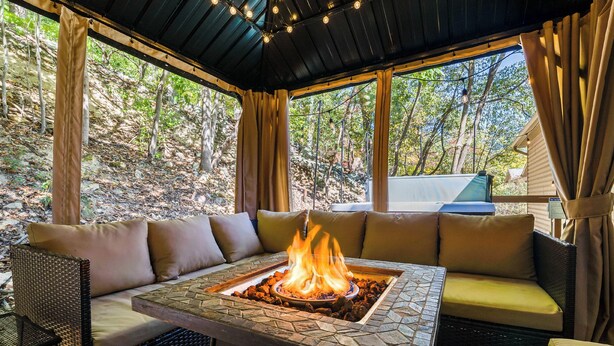 A covered outdoor seating area with a fire feature, cushioned sofas, and a table.