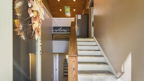 A staircase with wooden steps and a wooden handrail, leading to a room with a 'welcome' sign and a 'Mountain Mindset' sign.