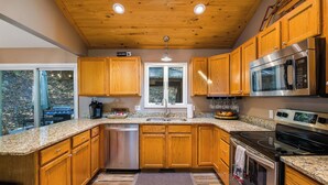 A modern kitchen with wooden cabinets, stainless steel appliances, and a window overlooking a garden.