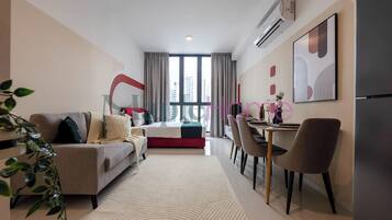 Una sala de estar moderna con un sofá, una mesa de comedor con sillas, un ventanal con cortinas y vistas a edificios.