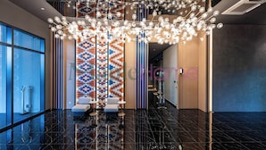 Un vestíbulo moderno con piso de mármol negro, un muro con diseño geométrico y colorido, y una araña.