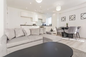 Un soggiorno moderno con un divano componibile, un'area pranzo con tavolo e sedie, e una cucina sullo sfondo.