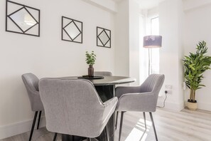 Un'area pranzo moderna con un tavolo rotondo, quattro sedie grigie e tre opere d'arte geometriche a parete.