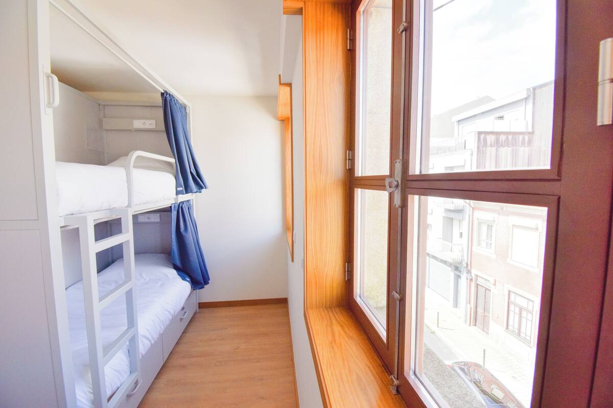 Ein Zimmer mit Etagenbetten, einem Fenster und Blick auf Gebäude.