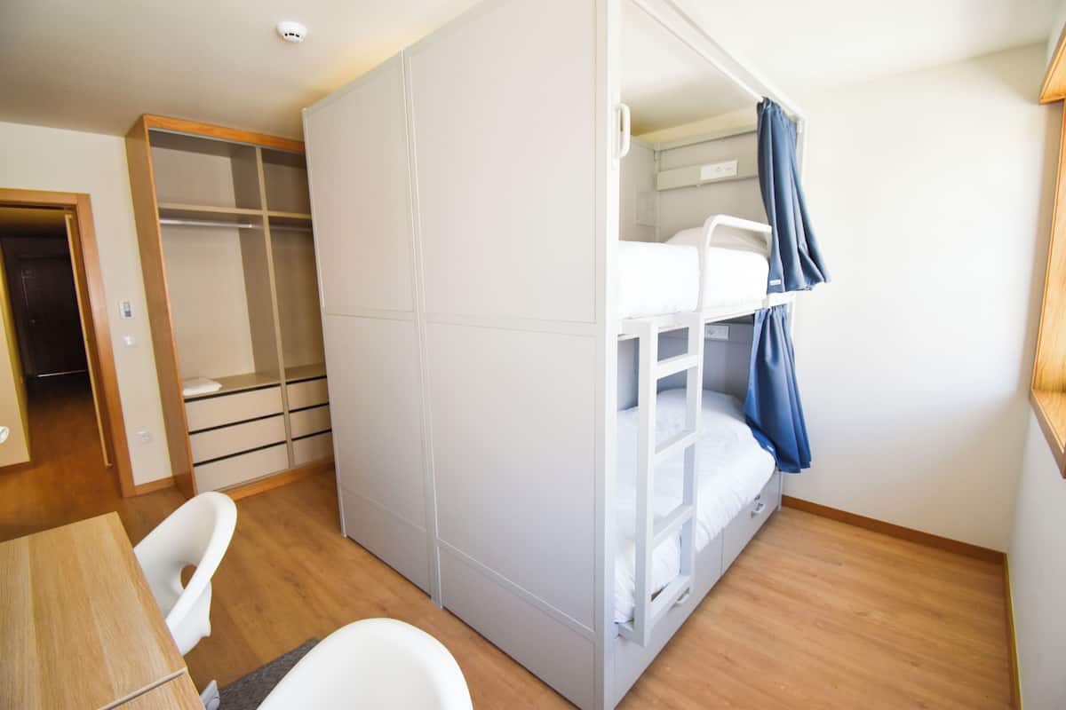Ein Zimmer mit Etagenbett, Schreibtisch, Stuhl und Kleiderschrank.