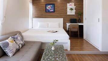 A modern hotel room with a bed, a sofa, a small table with a plant, a desk with a chair, and a wooden wall.
