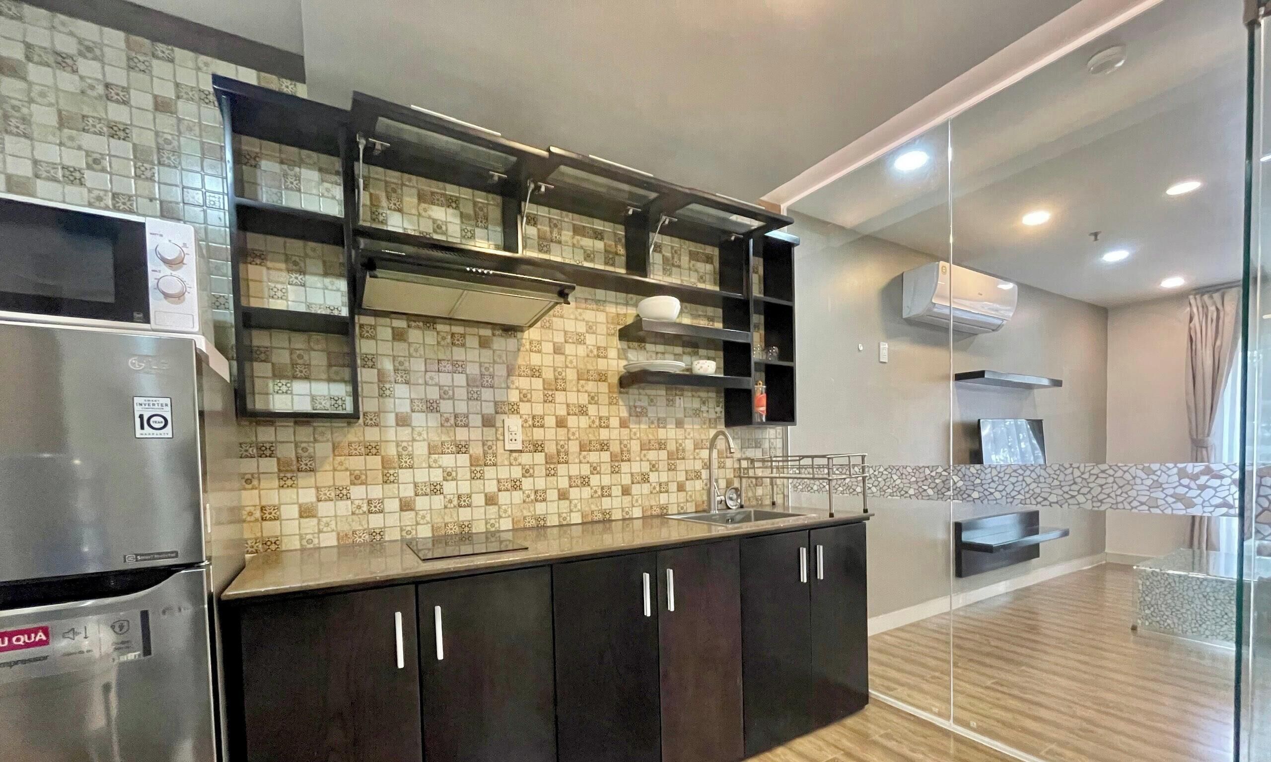 A modern kitchen with dark cabinets, a stainless steel refrigerator, and a tiled backsplash.