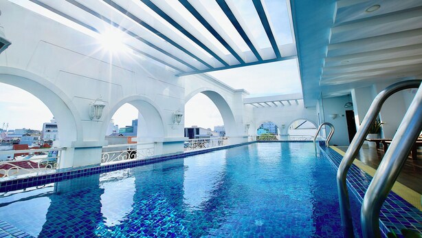 An indoor swimming pool with clear blue water, white arches, and a view of the cityscape through the ceiling. - 5H - SaiGon Huch Villa by SAVIHOUSE (Ho Chi Minh City)