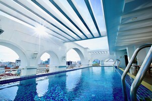 An indoor swimming pool with clear blue water, white arches, and a view of the cityscape through the ceiling.