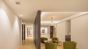 A modern hallway with green armchairs and a small table, leading to a room with a framed artwork and a door labeled "16". - Mon Suites Jardín de Ayora (València)