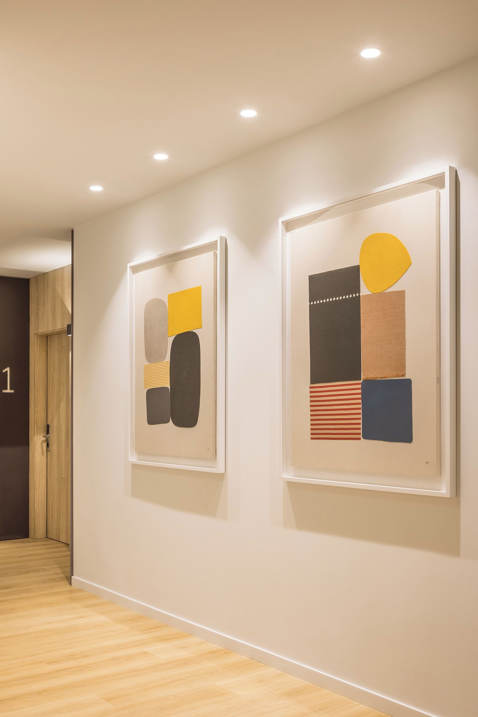 A hallway with two framed abstract artworks on the wall and a wooden floor.
