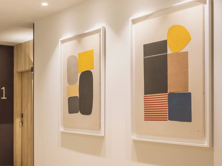 A hallway with two framed abstract artworks on the wall and a wooden floor.