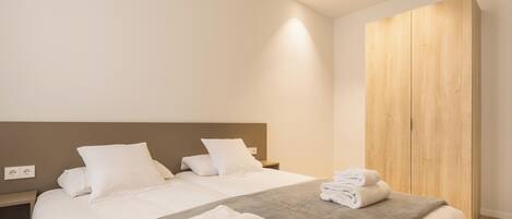 A modern hotel room with a large bed, a wooden wardrobe, and a bedside table.