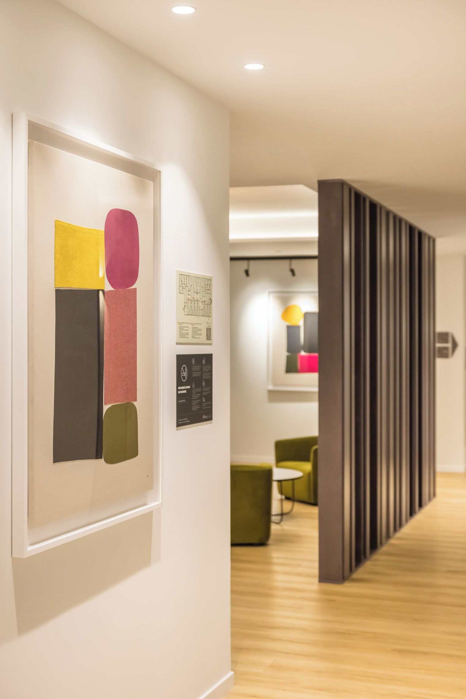Ein modernes Interieur mit Holzboden, einem gerahmten abstrakten Kunstwerk und einer Sitzecke mit einem grünen Sessel und einem kleinen Tisch.