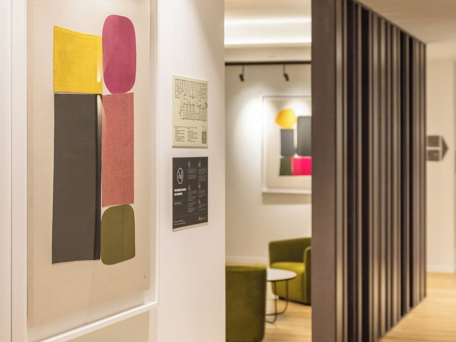 Un intérieur moderne avec un plancher en bois, une œuvre d’art abstraite encadrée et un coin salon comprenant un fauteuil vert et une petite table.