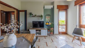 Een moderne woonkamer met een televisie, een eettafel en een bank. Er staan planten en een fotokader aan de muur.