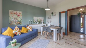 Ein Wohnzimmer mit blauem Sofa, einem Esstisch mit Stühlen und einer Küche im Hintergrund.
