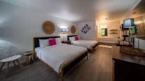 A hotel room with two beds, a small table, a TV, and a kitchenette.