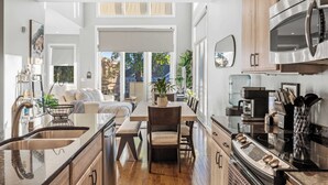 A modern kitchen with a dining area, wooden cabinets, stainless steel appliances, and a large window providing natural light. - NEW Elegant Downtown Escape with Modern Comforts (Louisville)