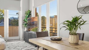 A modern dining area with a large table, chairs, a potted plant, and a view of a cityscape through large windows. - NEW Elegant Downtown Escape with Modern Comforts (Louisville)