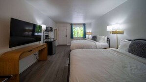 Une chambre d’hôtel avec deux lits, une télévision, un bureau et une fenêtre avec des rideaux.