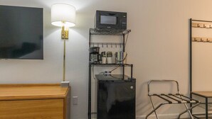Ett kompakt hotellrum med en byrå i trä, ett svart kylskåp, en mikrovågsugn på en hylla i metall, ett litet bord, en stol och en väggmonterad TV.
