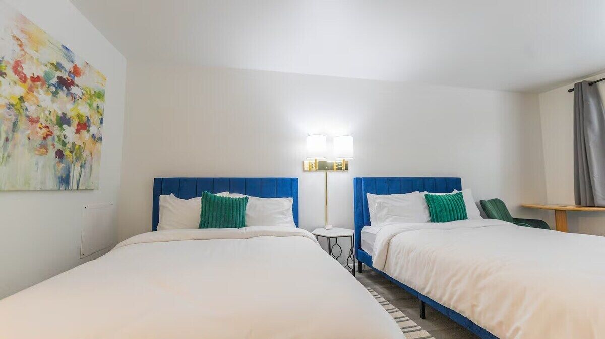 A hotel room with two beds, a small table, and a lamp.