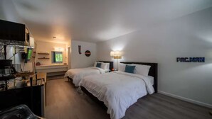 A hotel room with two beds, a desk, a chair, a TV, and a wall-mounted lamp.