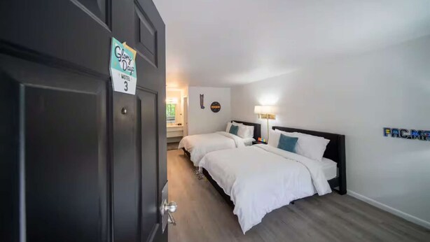 A hotel room with two beds, a nightstand, a lamp, and a sign indicating the room number.