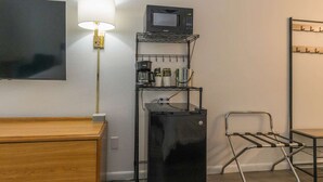 A hotel room with a wooden dresser, a flat-screen TV, a lamp, a coffee machine, a microwave, a refrigerator, and a metal chair. - KC Room, #7 at Glory Dayz! (Eureka Springs)