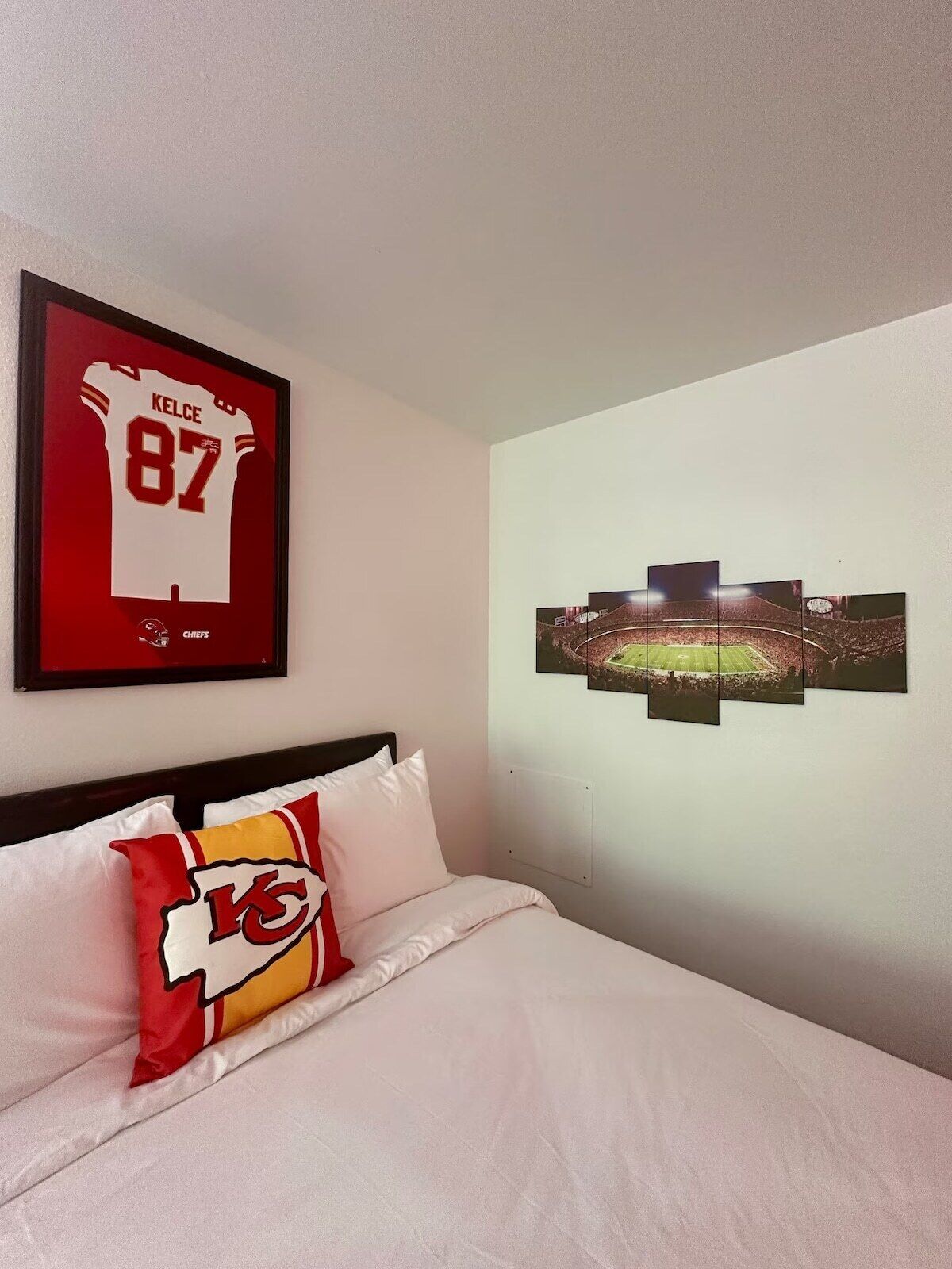 A hotel room with a bed, a framed jersey, and a stadium mural.