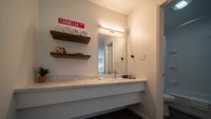 A bathroom with a white vanity, a mirror, and a shower area. - Lucky #13, room at Glory Dayz! (Eureka Springs)