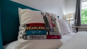 A bed with a pillow featuring book titles. - Lucky #13, room at Glory Dayz! (Eureka Springs)