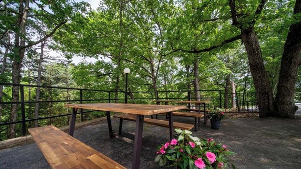 An outdoor wooden picnic table with benches, surrounded by a metal fence, set in a forested area with trees and a gravel ground. - Lucky #13, room at Glory Dayz! (Eureka Springs)